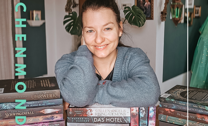 Autorin lächelnd auf dem Bücherstapel, der beim Drachenmond Verlag erschienen ist.